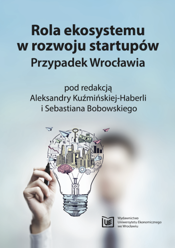 Błękitno-szara okładka, na górze czarną czcionką tytuł, poniżej ręka rysująca żarówkę w środku której znajduje się nowoczesne miasto.